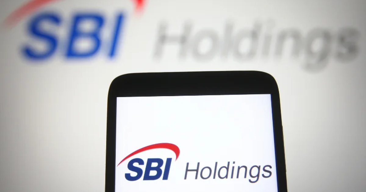SBIホールディングスのロゴが表示されたスマートフォンと、背景にぼかしたSBI Holdingsのロゴが写った写真